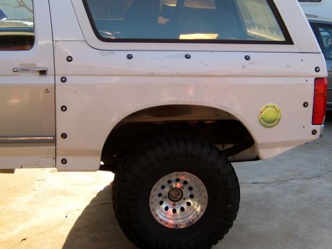 1996 Ford Bronco - Rear quarter view of a white two-door Ford Bronco SUV with a fuel filler door, oversized mud-terrain tire and polished aluminum beadlock-st…