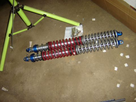 1992 Ford Bronco - Two coilover shock absorbers, one with red springs and one with silver springs, are laid out on a concrete floor.