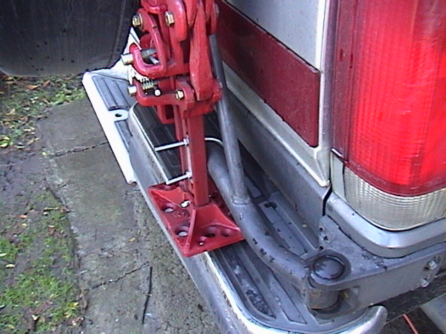 Red hi-lift jack mounted on rear bumper of a vehicle