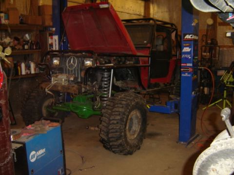 1992 Ford Bronco - A heavily modified off-road vehicle is undergoing repairs in a workshop, with its hood raised to reveal the engine bay.