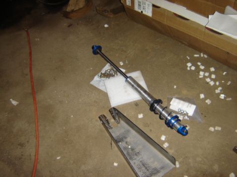 1992 Ford Bronco - A shock absorber and a suspension component are laid out on a concrete floor, possibly for installation or repair.