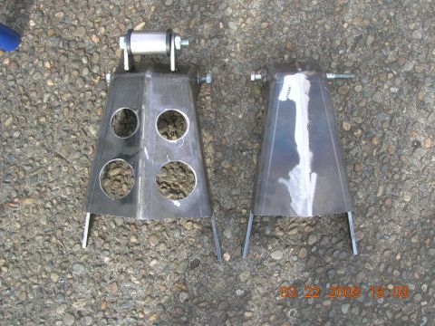1996 Ford Bronco - Two custom metal brackets, one with four circular holes and a roller assembly, are shown on a gravel surface.