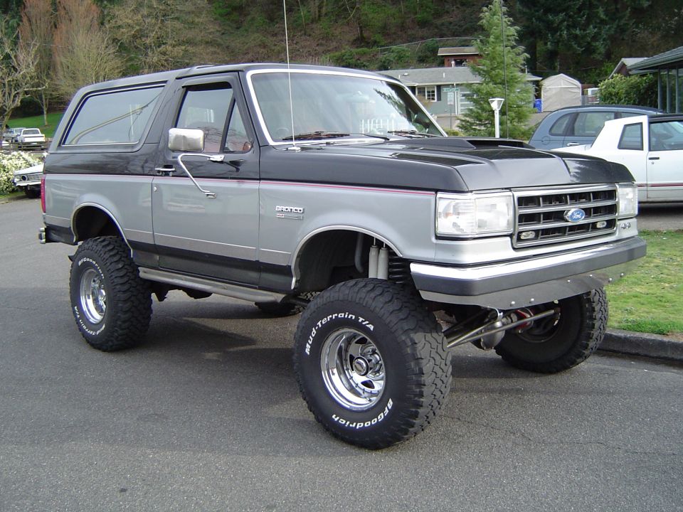 Lifted black and silver Ford Bronco with hood scoop and BFGoodrich Mud-Terrain tires on a street