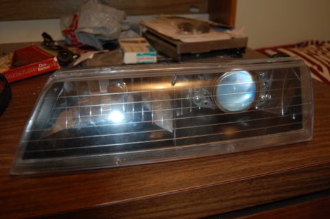 1985 Mercury Grand Marquis - Headlight assembly with a projector retrofit is shown on a wooden surface.