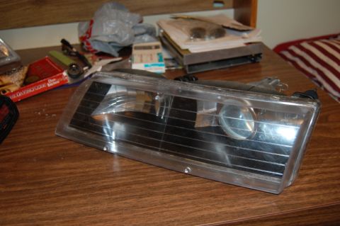 1985 Mercury Grand Marquis - Headlight assembly shown on a table, with various items in the background.