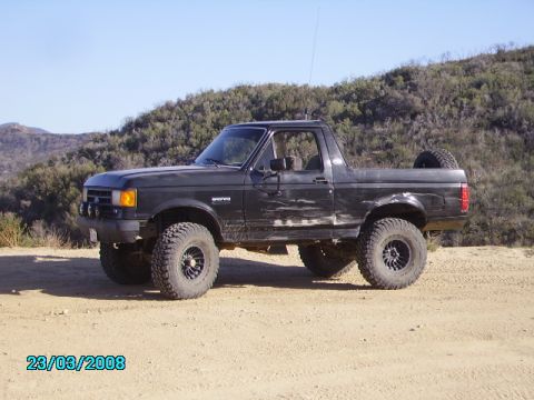 1990 Ford Bronco - This black Ford Bronco is parked on a dirt road with hills in the background.