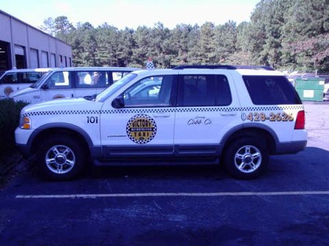 1996 Ford Crown Victoria - A white SUV taxi is parked in a lot next to another taxi.
