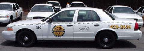 1996 Ford Crown Victoria - A fleet of white taxi cabs are parked together, with one prominent in the foreground showing its identification number and service details.