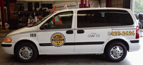 1996 Ford Crown Victoria - This white minivan taxi displays "Victory Taxi" and a phone number on its side.