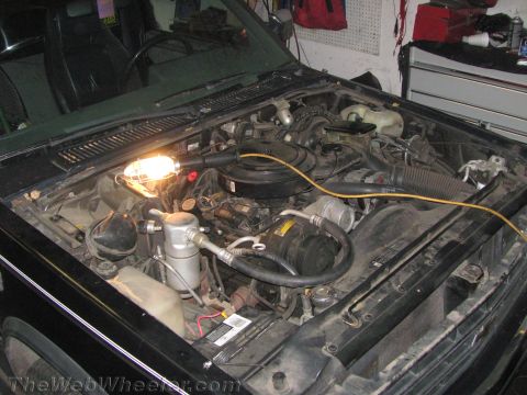 1987 Suzuki Samurai - The engine bay of a vehicle is illuminated by a work light, showing various mechanical parts and wiring.