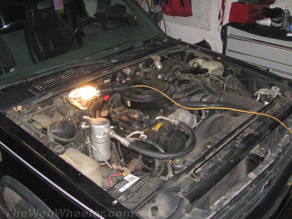 engine bay with work light on engine components, hoses, and battery