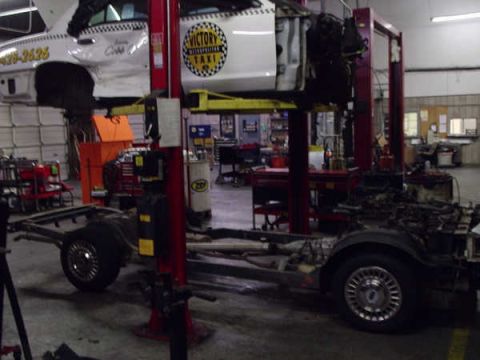 1996 Ford Crown Victoria - A taxi is undergoing repairs in a garage, with its body elevated and chassis accessible.