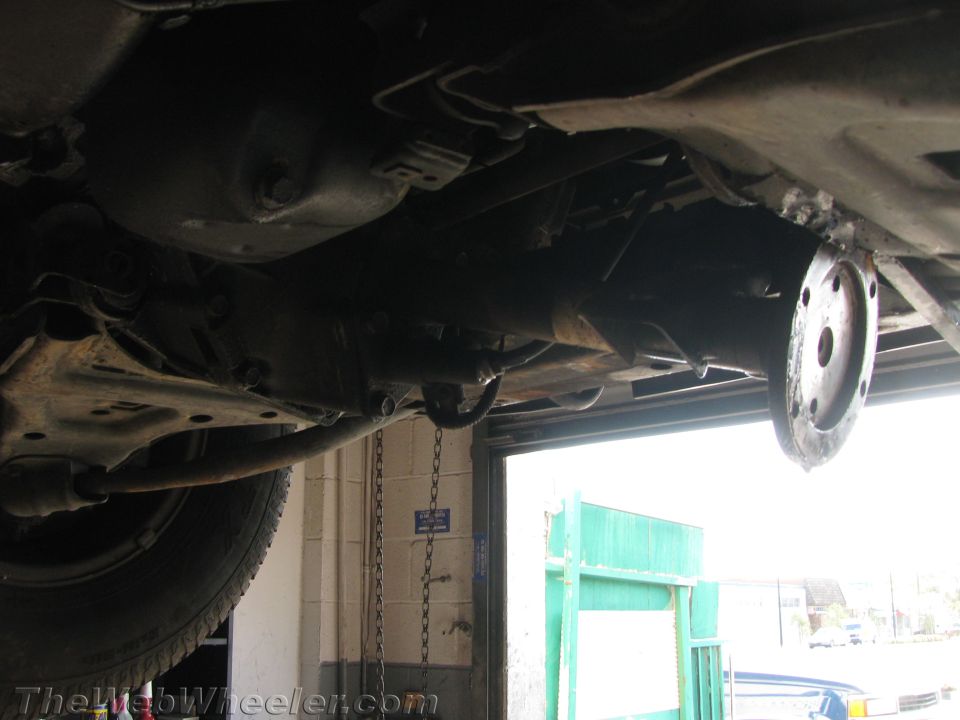 Underside view of a vehicle's drivetrain, showing the transmission and driveshaft. A flange is visible on the right