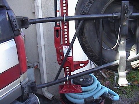 1990 Ford Bronco - Hi-Lift jack mounted on a vehicle's spare tire carrier, with a blue hose visible.