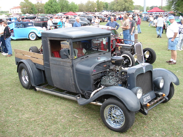 Custom hot rod pickup truck with exposed engine and wooden bed, parked on grass at a car show