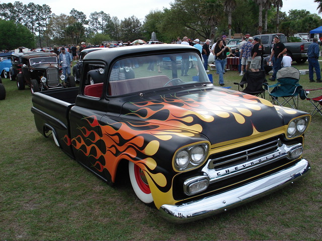 Black 1959 Chevrolet pickup truck with orange and yellow flames, lowered stance, and whitewall tires