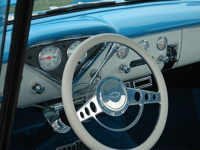 Interior view of a car with a white steering wheel, chrome horn button with Chevrolet logo, and multiple gauges on the dashboard