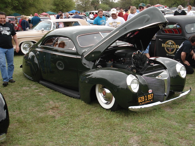 Dark green coupe with hood open, white wall tires, chrome bumper, and California license plate 6ZB 1 997