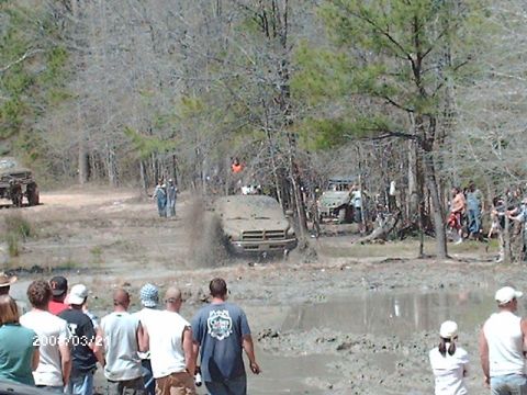 1990 Ford F-150 - A truck navigates a muddy course during an off-road event, with onlookers gathered to observe the action.