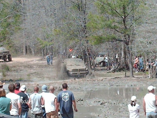 Muddy truck splashing through a bog with spectators watching