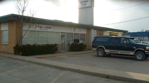1995 Ford C-350 (Centurion Conversions) - A dark blue 1995 Ford C-350 Centurion Conversions SUV is parked in front of a commercial building with several businesses.