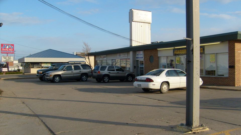 Commercial buildings and parking lot with several cars including a white sedan and SUVs