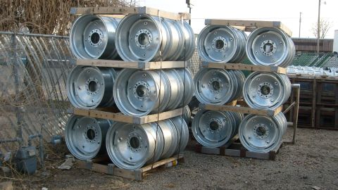 1995 Ford C-350 (Centurion Conversions) - Multiple stacks of silver metal wheels are stored outdoors on wooden pallets.