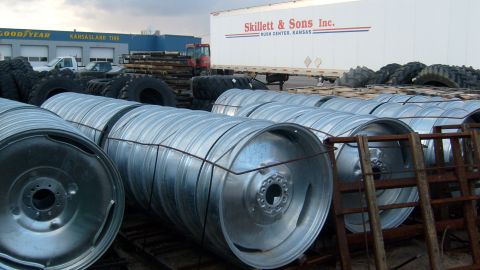 1995 Ford C-350 (Centurion Conversions) - A tire shop lot displays stacks of large metal rims alongside a semi-trailer and piles of tires.