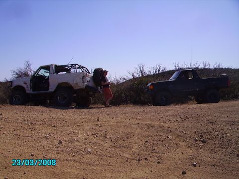 1990 Ford Bronco - Two vehicles are parked on a dirt road with a person loading gear onto the white SUV.