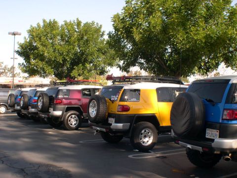 2007 Toyota FJ Cruiser - Multiple Toyota FJ Cruisers are parked in a lot under trees on a sunny day.