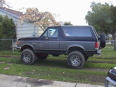 1990 Ford Bronco - This Ford Bronco is parked on a grassy area next to a building and fence.