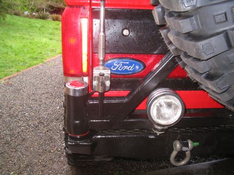 1989 Ford Bronco - The rear of a red Ford Bronco features a black custom bumper with a spare tire mount and auxiliary lights.