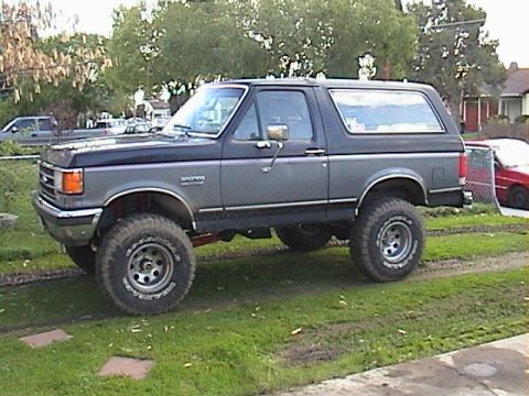 1990 Ford Bronco - This lifted Ford Bronco is shown from the side, large tires and a two-tone paint scheme.