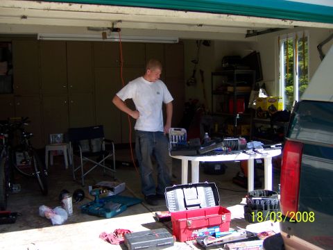 1991 Ford Bronco - A young man stands in a cluttered garage with tools and equipment spread around.