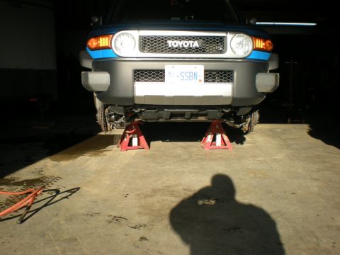 2007 Toyota Land Cruiser - A blue Toyota FJ Cruiser is elevated on red jack stands in a garage, showing its front grille and bumper.