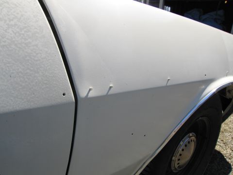 1991 Ford LTD Crown Victoria - Close-up of a white car's side panel shows multiple screw holes and a section of chrome trim.