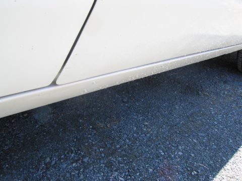 1991 Ford LTD Crown Victoria - Close-up of the lower side panel of a white vehicle, showing a detail line and gravel on the ground.