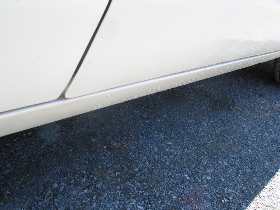 Side view of a white car's lower body panel with gravel on the ground