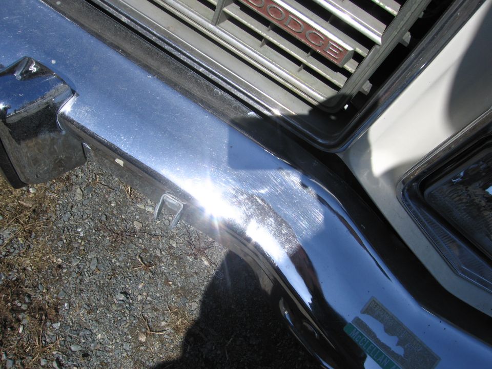 Chrome bumper with a dent and a Dodge grille above it. Green sticker on bumper