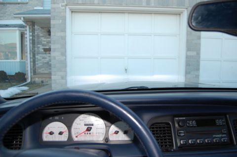 1985 Mercury Grand Marquis - Dashboard view from inside a car, looking out at a garage door. Gauges suggest a 1998 model year.