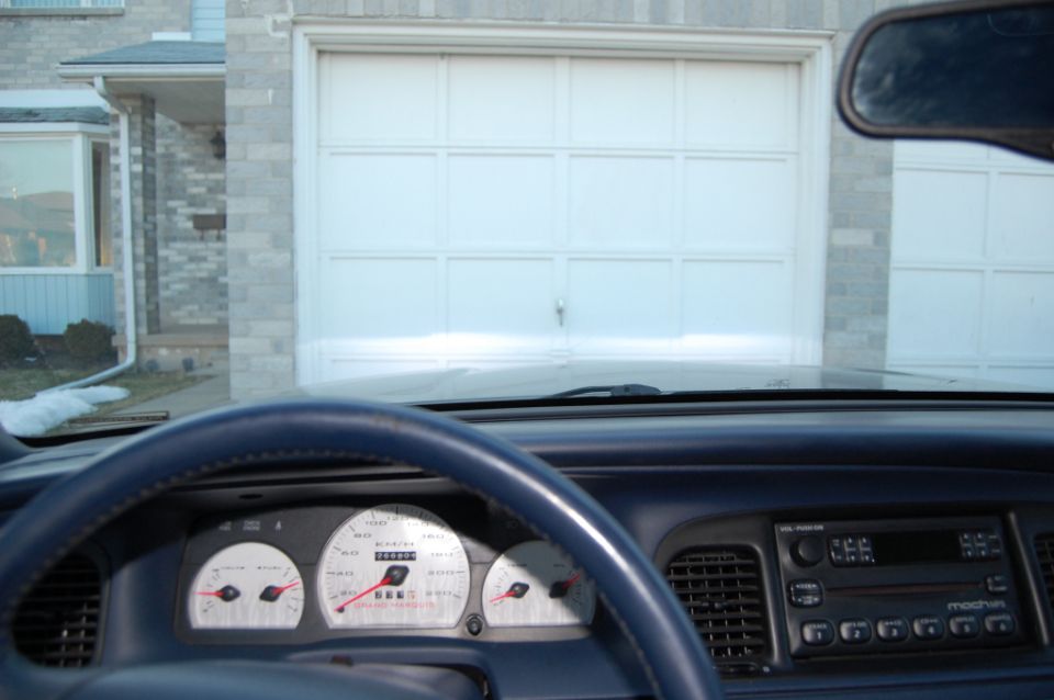 Car interior with white gauges, steering wheel, radio, garage seen through windshield