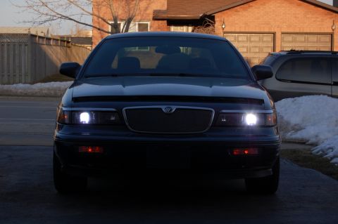 1985 Mercury Grand Marquis - Dark Mercury Grand Marquis parked outside with headlights illuminated.