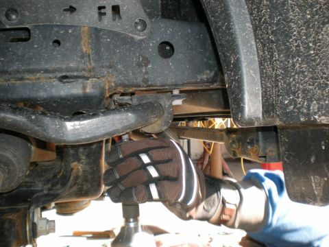 2007 Toyota Land Cruiser - Close-up of a vehicle's front suspension system, with a hand using a tool on a bolt. The 'FR' marking is visible on the frame.