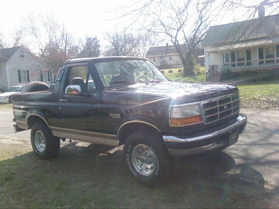 Black Ford Bronco with top removed, parked in driveway, 3/4 front view