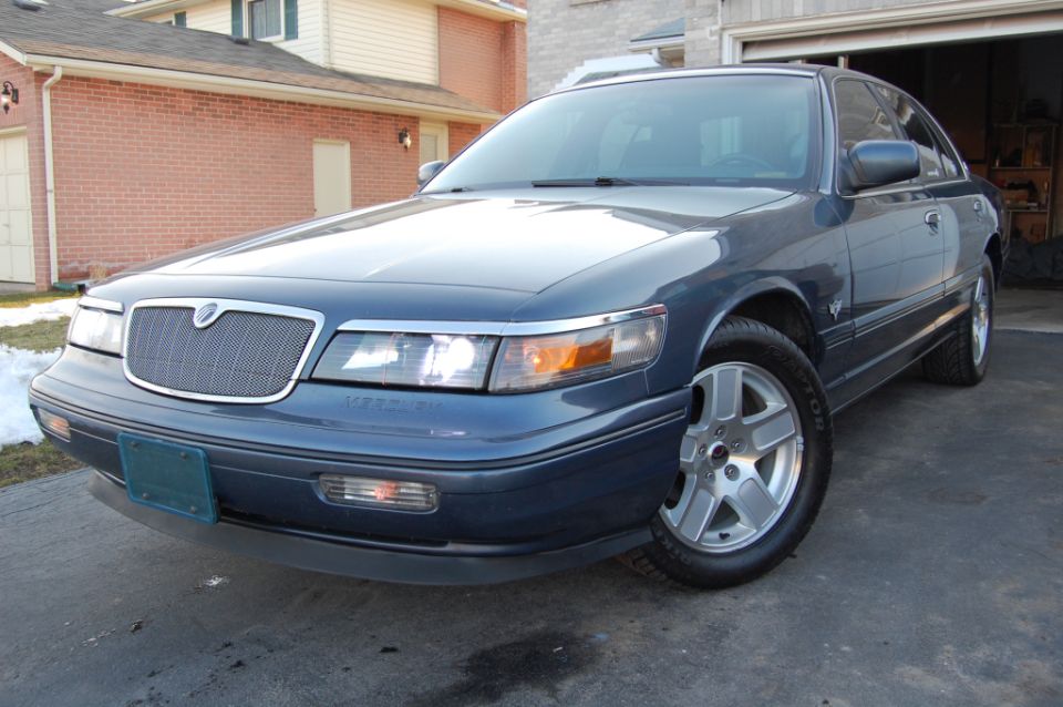 Blue Mercury sedan, front 3/4 view, on driveway by brick house