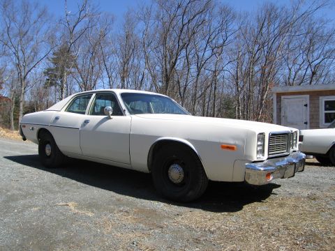 1991 Ford LTD Crown Victoria - A white 1977 Dodge Monaco sedan is parked on a gravel lot with trees and a shed in the background.