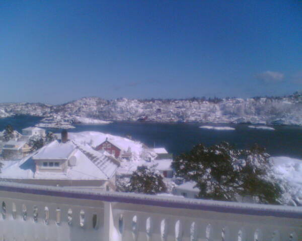 Snow-covered coastal town and blue fjord seen from a white balcony railing