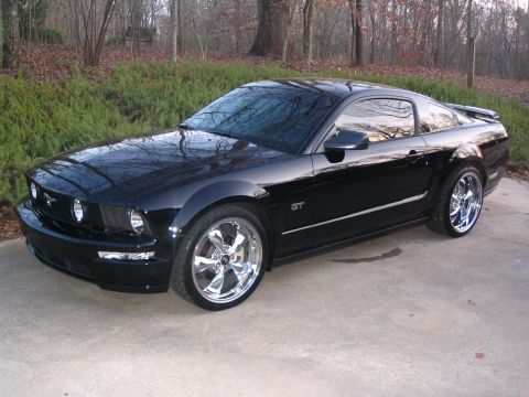 2007 Ford Mustang - A black Ford Mustang GT with custom chrome wheels is shown from a three-quarter front angle.