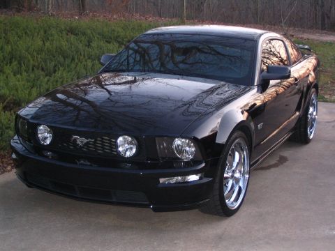 2007 Ford Mustang - A black 2007 Ford Mustang GT is parked on a concrete driveway, chrome wheels and a GT badge.