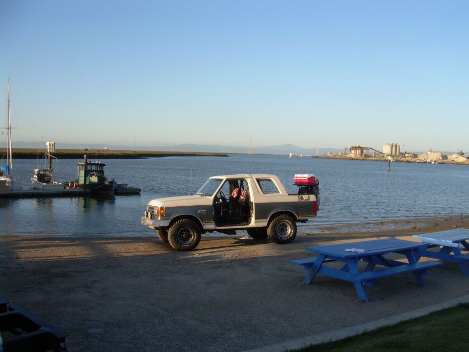 1991 Ford Bronco parked by water with doors open, red cargo box on spare tire